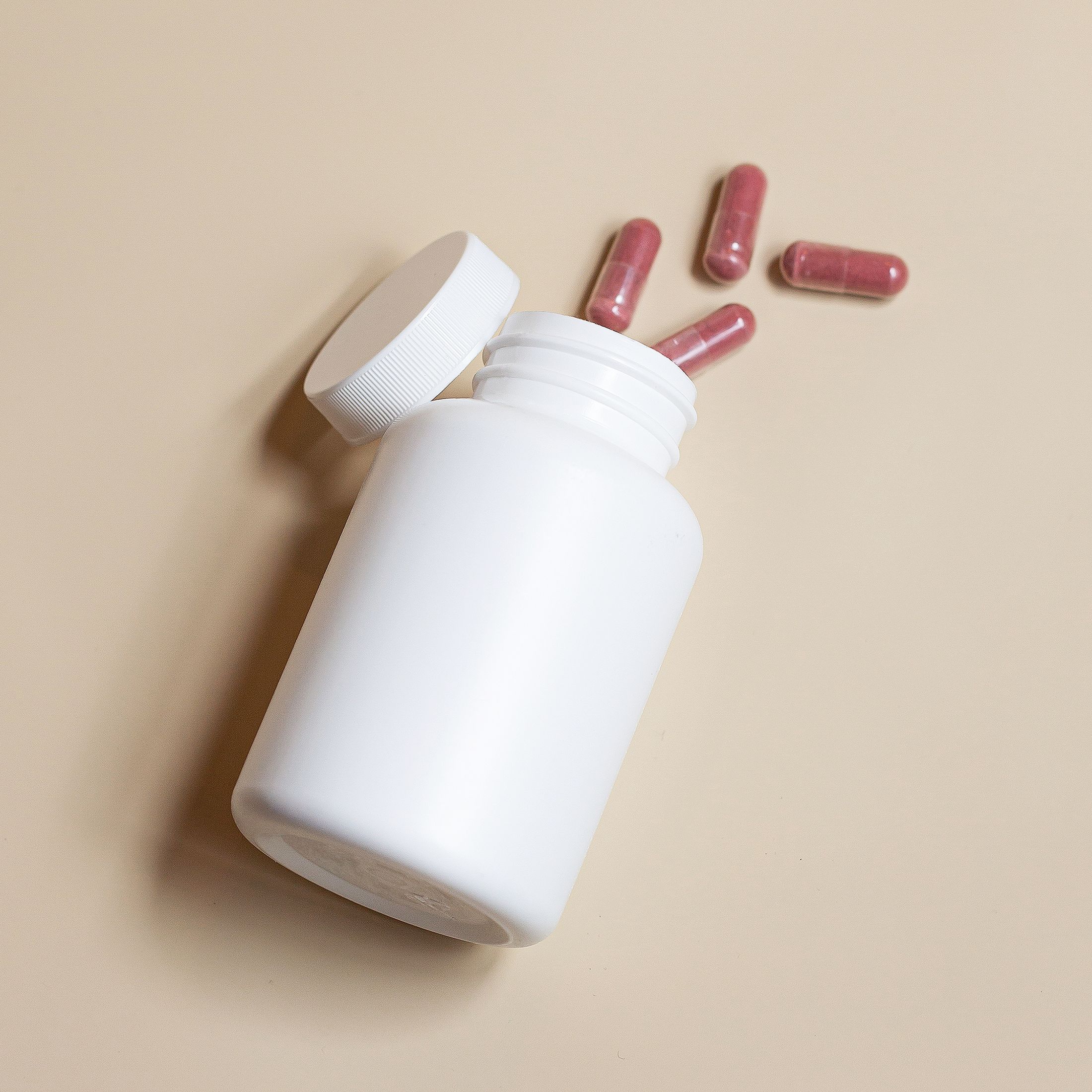 Unbranded capsule bottle and capsules on a neutral surface